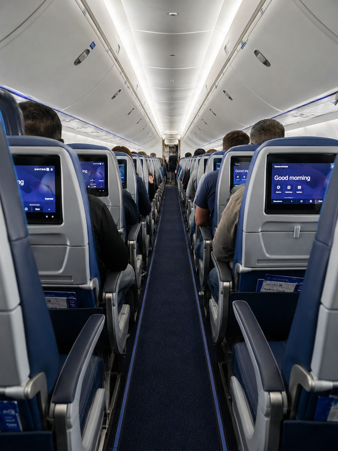 Looking down the aisle of a United economy cabin with rows of seatback screens showing the United interface — the seats PlusPoints let you upgrade out of